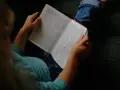 Dziecko w niebieskiej koszulce trzyma otwartą Biblię, przygotowując się do modlitwy przed czytaniem Pisma Świętego.