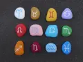 Kolorowe kamienie z symbolami zodiaku ułożone w rzędach. Widoczny jest znak zodiaku przed Koziorożcem, czyli Strzelec.