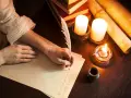Ręka pisze piórem prośbę do anioła stróża. W blasku świec, wśród starych ksiąg i zwojów, powstaje list.