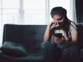 Zmartwiona kobieta siedzi na kanapie, trzymając telefon. Czyta wiadomości, które mogą dotyczyć jej związku z rakiem i wagą.