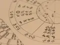 Zbliżenie na wykresy astrologiczne z symbolami planet i znaków zodiaku. Widoczny fragment horoskopu, gdzie 22.11 to znak zodiaku Strzelec.