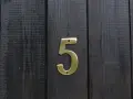Złota cyfra 5 na ciemnej, drewnianej desce. Numerologiczna 3 i 5 symbolizują zmianę i wolność.