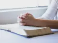 Dłonie złożone w modlitwie nad otwartą Biblią. To chwila głębokiej wiary i modlitwa o zdrowie dziecka.