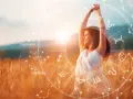 Kobieta w białej sukience cieszy się słońcem na polu. Wokół niej krąg znaków zodiaku, symbolizujący numerologię codzienną.