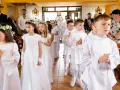 Dzieci w białych strojach, dziewczynki z wiankami, chłopcy z medalikami, przygotowują się do przyjęcia sakramentu, co to jest komunia święta.
