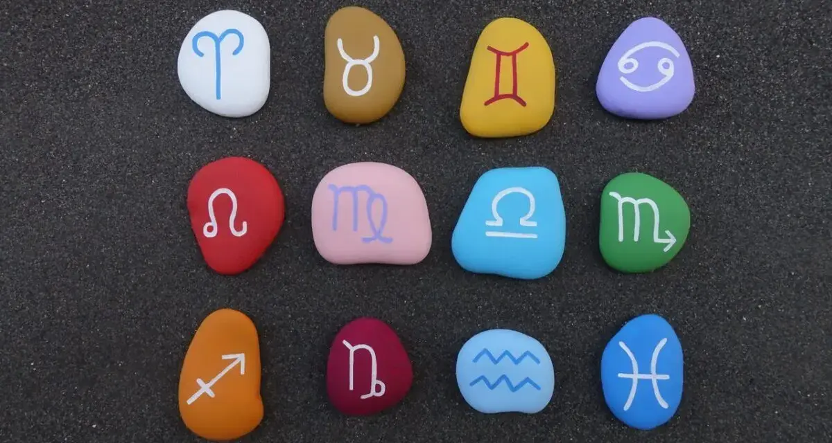 Kolorowe kamienie z symbolami zodiaku ułożone w rzędach. Widoczny jest znak zodiaku przed Koziorożcem, czyli Strzelec.