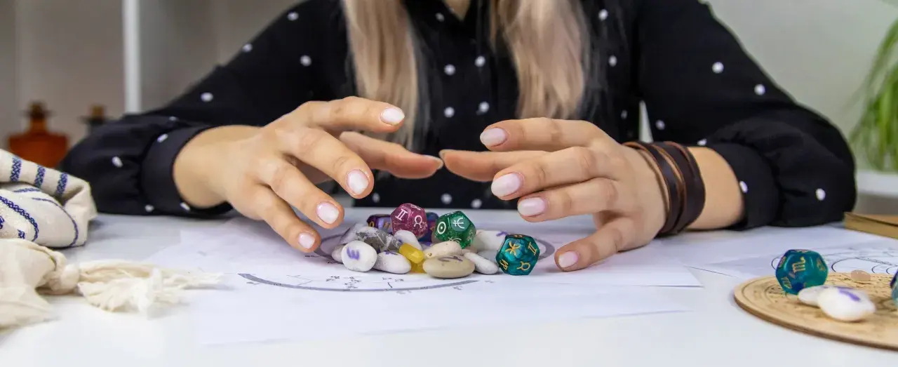 Dłonie nad kamieniami i kostkami z symbolami zodiaku. Czy wśród nich kryje się najsilniejszy znak zodiaku?