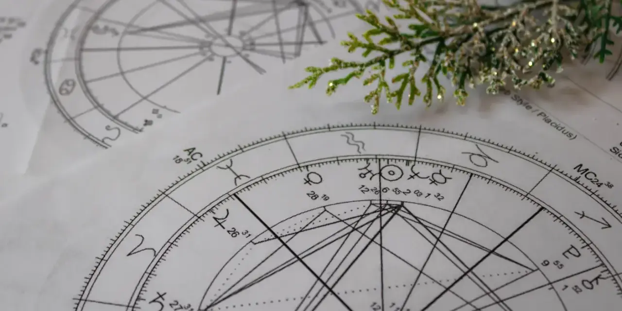 Złożone wykresy astrologiczne, kluczowe dla nauki o znakach zodiaku, leżą na stole, ozdobione gałązką.