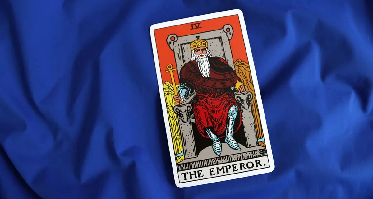 Karta cesarz tarot, przedstawiająca władcę na tronie, leży na niebieskim tle.