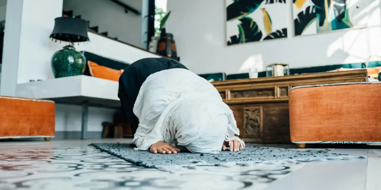 Kobieta w hidżabie klęczy na dywaniku, wykonując modlitwy o pokój. W tle widać nowoczesne wnętrze z dziełami sztuki.