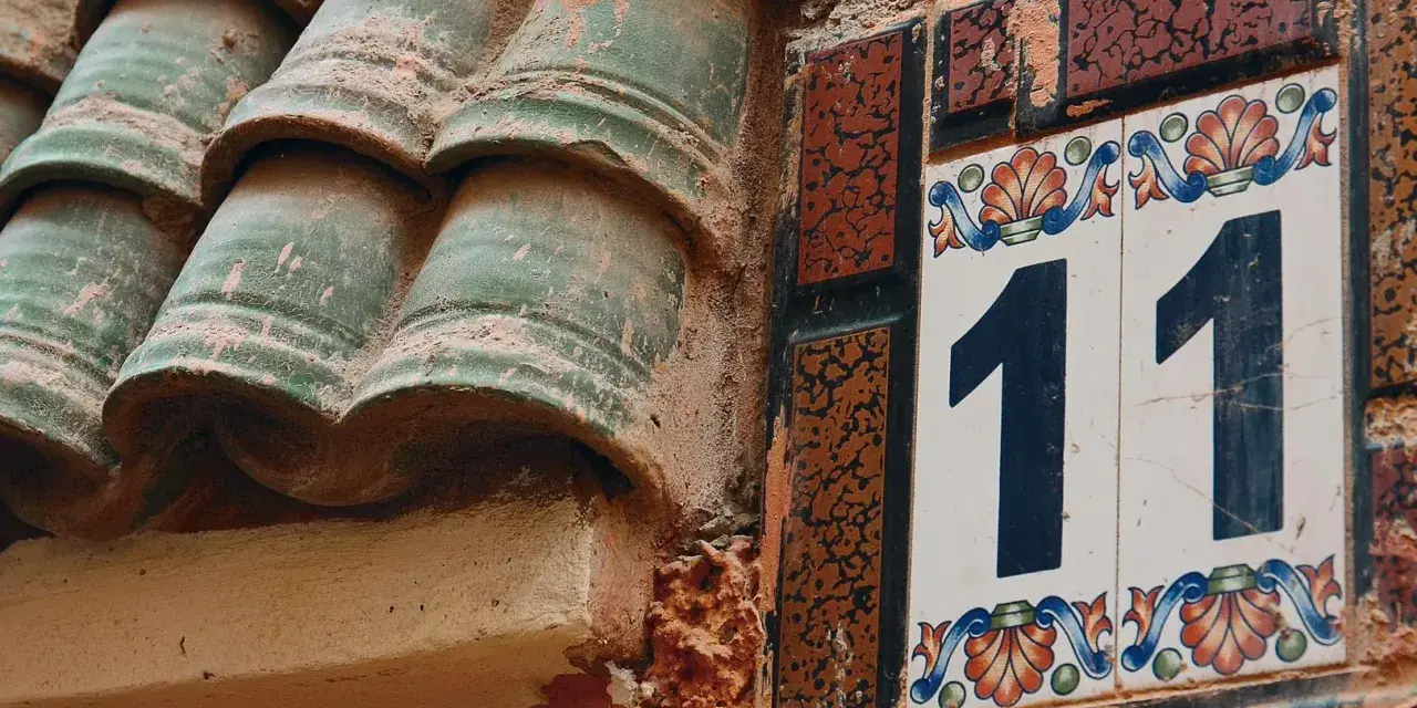 Numerologia partnerska 11 i 11. Dwa numery 11 na ozdobnych kafelkach, obok zielonych dachówek.