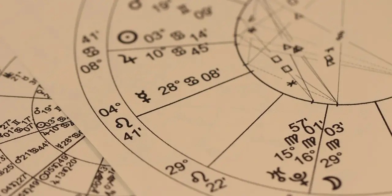 Zbliżenie na wykresy astrologiczne z symbolami planet i znaków zodiaku. Widoczny fragment horoskopu, gdzie 22.11 to znak zodiaku Strzelec.