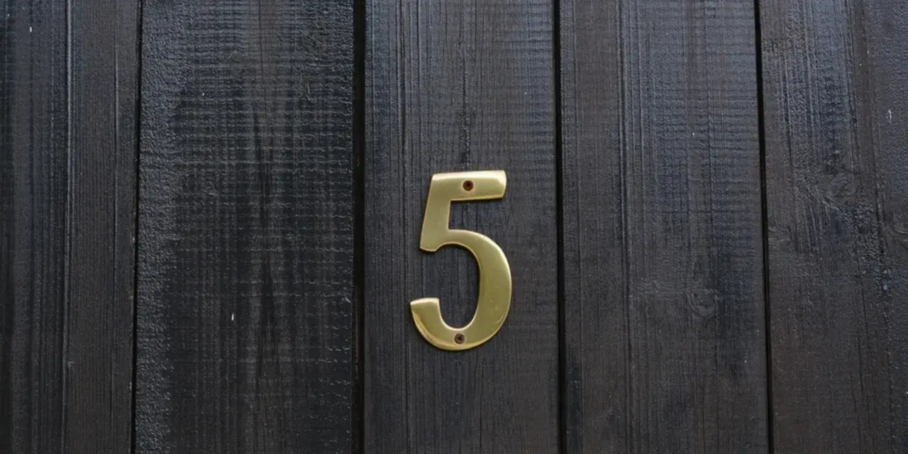 Złota cyfra 5 na ciemnej, drewnianej desce. Numerologiczna 3 i 5 symbolizują zmianę i wolność.
