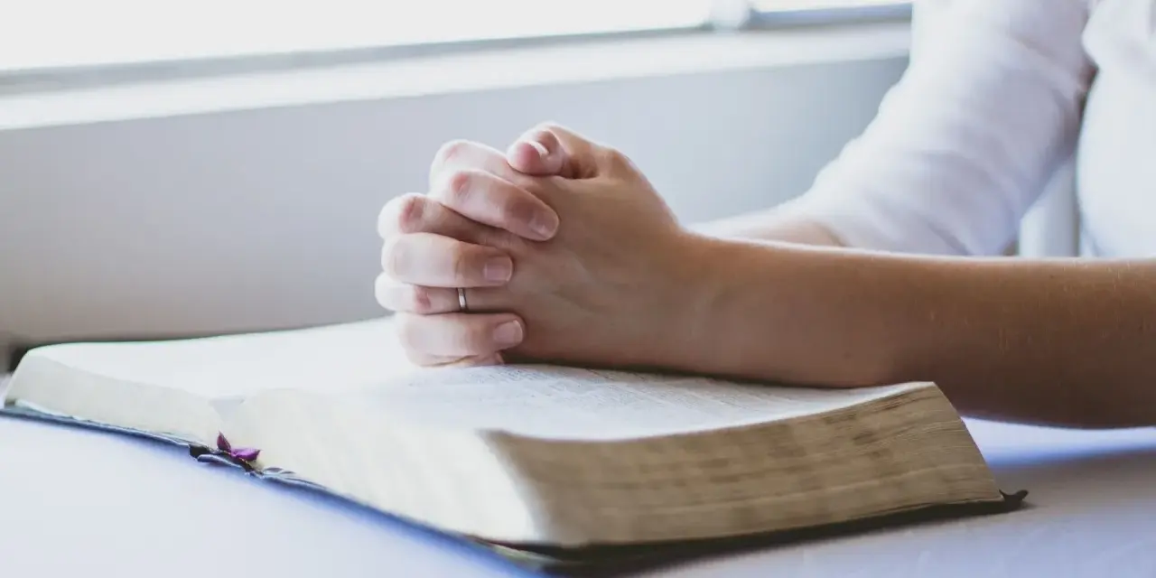 Dłonie złożone w modlitwie nad otwartą Biblią. To chwila głębokiej wiary i modlitwa o zdrowie dziecka.