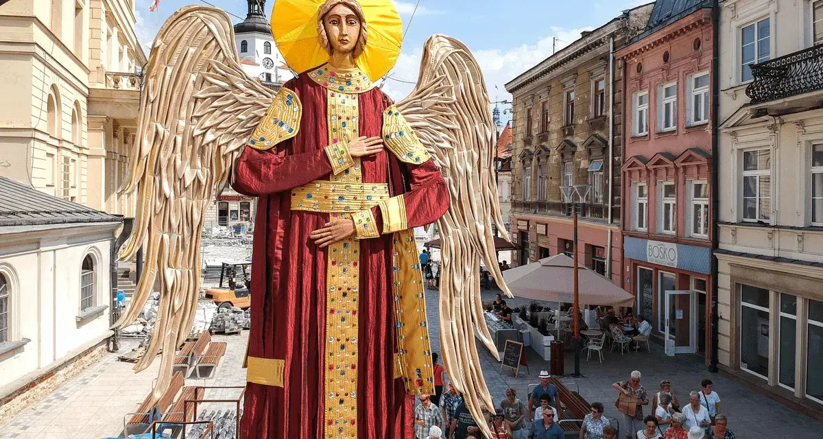 Gigantyczny Archanioł w czerwonej szacie z aureolą i złotymi skrzydłami, jakby wznosił modlitwę do archanioła. Ludzie spacerują ulicą.