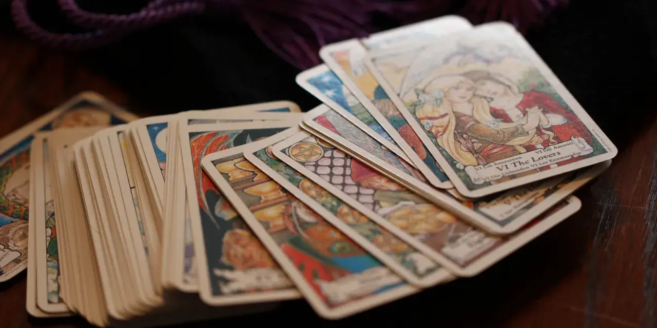 Karty tarota ułożone na drewnianym stole. Wśród nich widać kartę "Kochankowie". Sprawdź swój tarot tygodniowy skorpion.