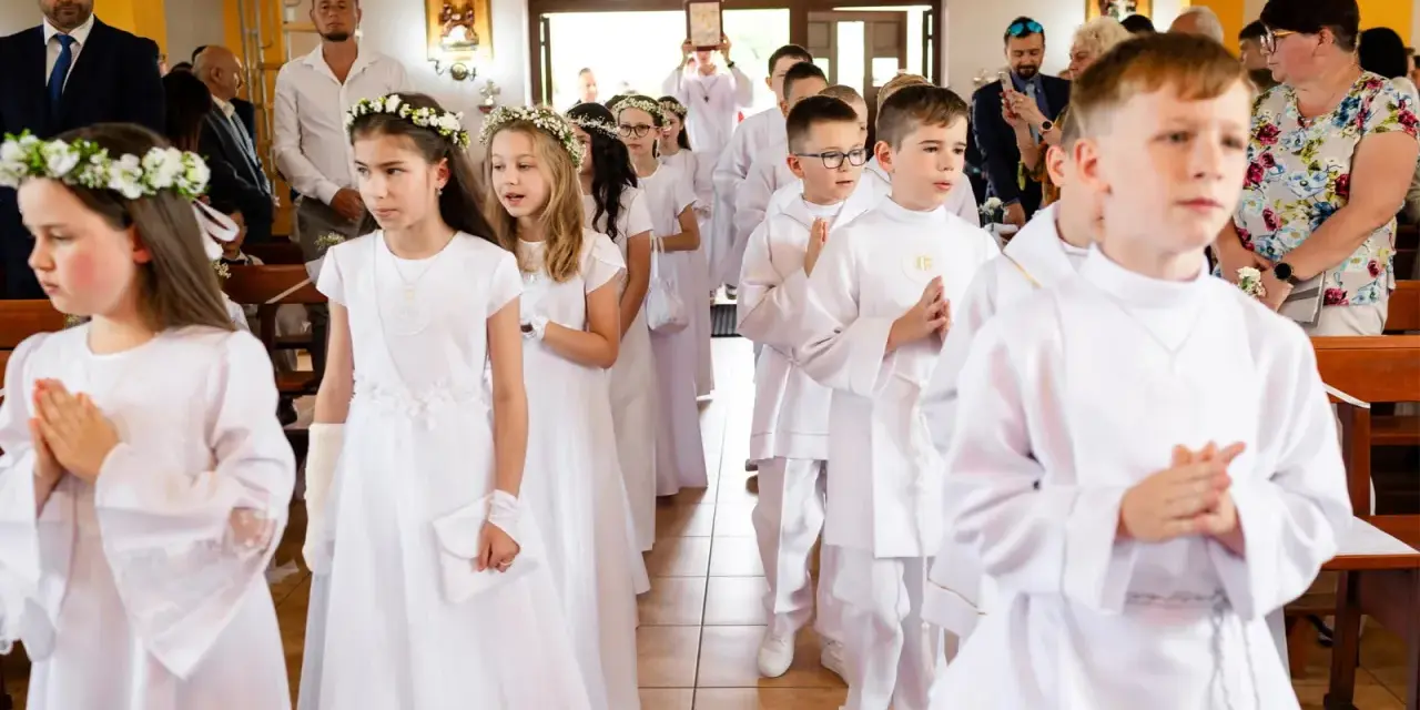 Dzieci w białych strojach, dziewczynki z wiankami, chłopcy z medalikami, przygotowują się do przyjęcia sakramentu, co to jest komunia święta.