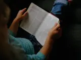 Dziecko w niebieskiej koszulce trzyma otwartą Biblię, przygotowując się do modlitwy przed czytaniem Pisma Świętego.