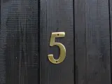 Złota cyfra 5 na ciemnej, drewnianej desce. Numerologiczna 3 i 5 symbolizują zmianę i wolność.