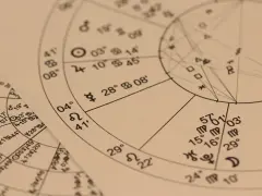 Zbliżenie na wykresy astrologiczne z symbolami planet i znaków zodiaku. Widoczny fragment horoskopu, gdzie 22.11 to znak zodiaku Strzelec.