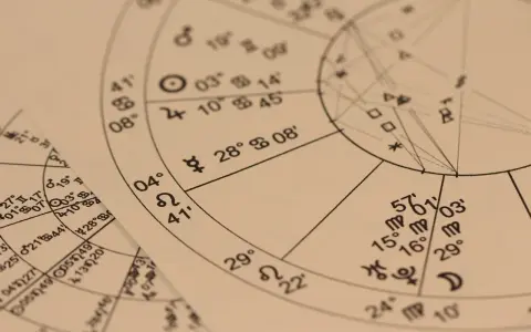 Zbliżenie na wykresy astrologiczne z symbolami planet i znaków zodiaku. Widoczny fragment horoskopu, gdzie 22.11 to znak zodiaku Strzelec.