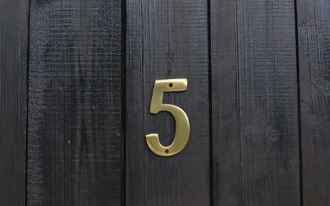 Złota cyfra 5 na ciemnej, drewnianej desce. Numerologiczna 3 i 5 symbolizują zmianę i wolność.