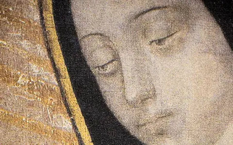 Zbliżenie na twarz z obrazu: łagodne oczy Matki Bożej z Guadalupe patrzą z ciemnego tła, otoczone złotym i czarnym obramowaniem.