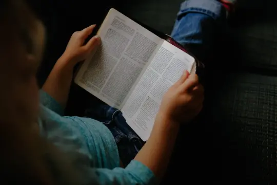 Dziecko w niebieskiej koszulce trzyma otwartą Biblię, przygotowując się do modlitwy przed czytaniem Pisma Świętego.
