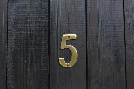 Złota cyfra 5 na ciemnej, drewnianej desce. Numerologiczna 3 i 5 symbolizują zmianę i wolność.