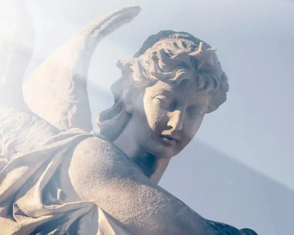 Kamienna rzeźba anioła, z promieniem światła padającym na twarz. Wzrok skierowany w dół, jakby w modlitwie do anioła stróża o pomoc.