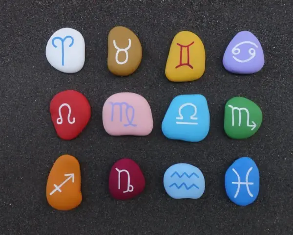 Kolorowe kamienie z symbolami zodiaku ułożone w rzędach. Widoczny jest znak zodiaku przed Koziorożcem, czyli Strzelec.