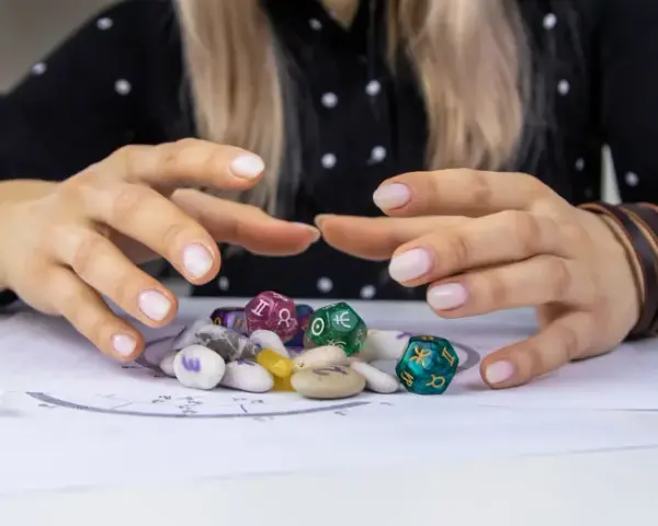 Dłonie nad kamieniami i kostkami z symbolami zodiaku. Czy wśród nich kryje się najsilniejszy znak zodiaku?