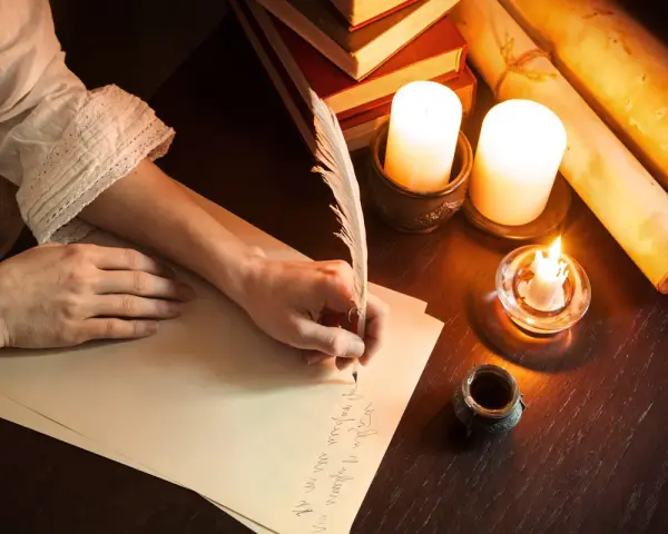 Ręka pisze piórem prośbę do anioła stróża. W blasku świec, wśród starych ksiąg i zwojów, powstaje list.