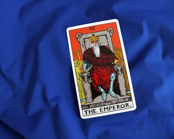 Karta cesarz tarot, przedstawiająca władcę na tronie, leży na niebieskim tle.