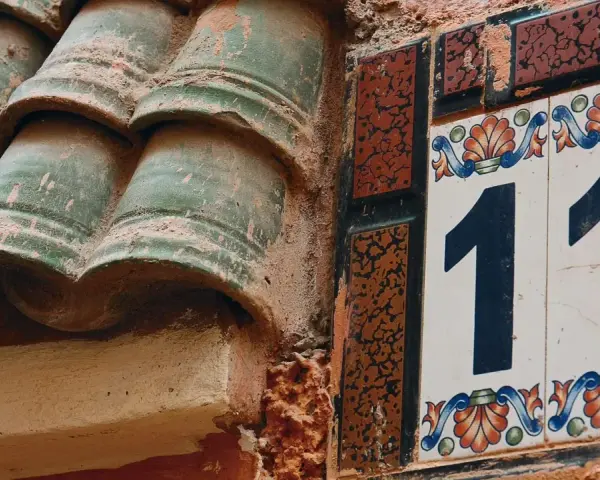 Numerologia partnerska 11 i 11. Dwa numery 11 na ozdobnych kafelkach, obok zielonych dachówek.