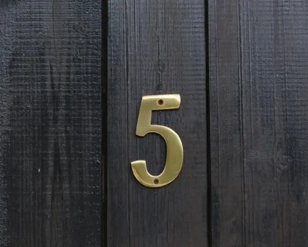 Złota cyfra 5 na ciemnej, drewnianej desce. Numerologiczna 3 i 5 symbolizują zmianę i wolność.