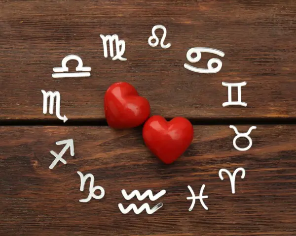 Dwa czerwone serca otoczone symbolami zodiaku, w tym znaki Wagi i Bliźniąt, na drewnianym tle.