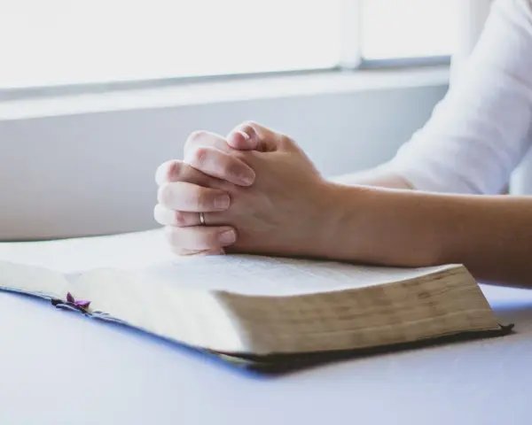 Dłonie złożone w modlitwie nad otwartą Biblią. To chwila głębokiej wiary i modlitwa o zdrowie dziecka.