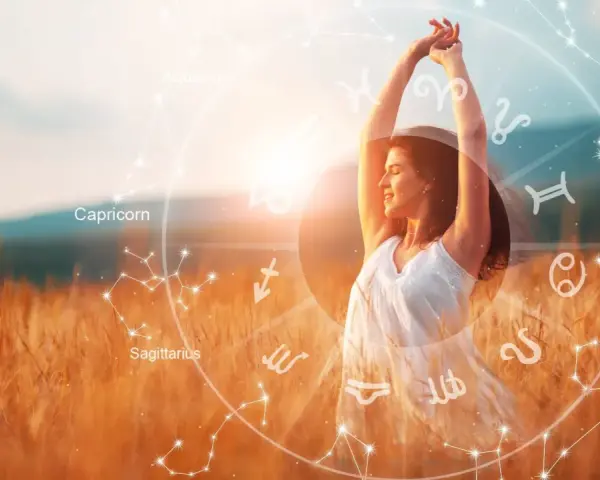 Kobieta w białej sukience cieszy się słońcem na polu. Wokół niej krąg znaków zodiaku, symbolizujący numerologię codzienną.