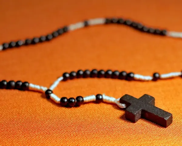 Różaniec z czarnymi i białymi paciorkami i drewnianym krzyżem. Symbolizuje modlitwę do anioła stróża.