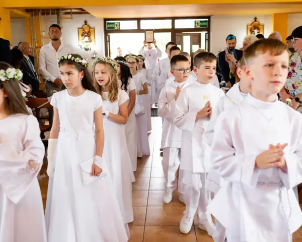 Dzieci w białych strojach, dziewczynki z wiankami, chłopcy z medalikami, przygotowują się do przyjęcia sakramentu, co to jest komunia święta.