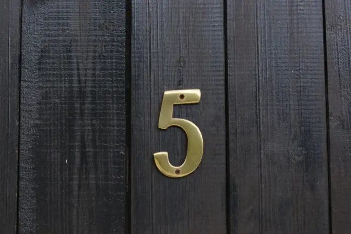 Złota cyfra 5 na ciemnej, drewnianej desce. Numerologiczna 3 i 5 symbolizują zmianę i wolność.
