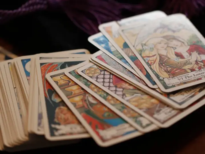 Karty tarota ułożone na drewnianym stole. Wśród nich widać kartę "Kochankowie". Sprawdź swój tarot tygodniowy skorpion.