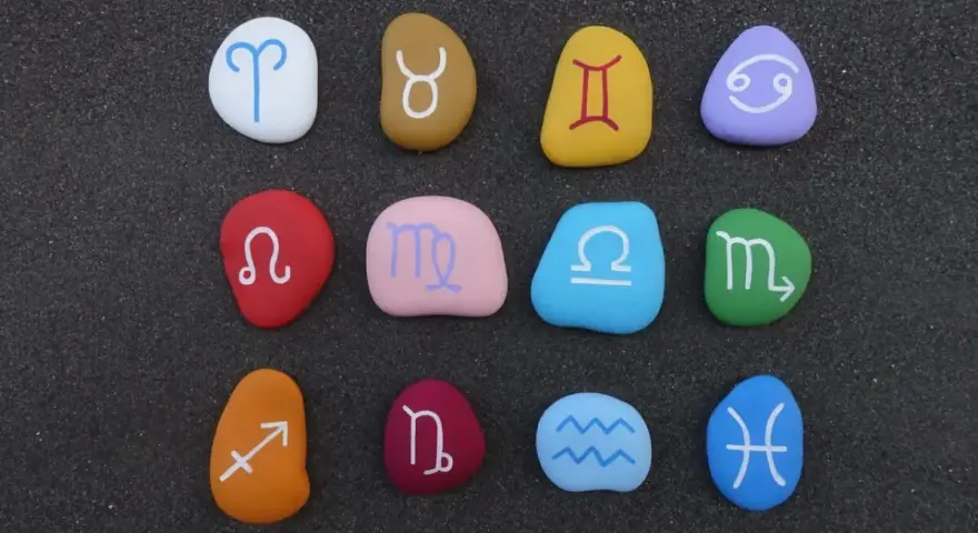 Kolorowe kamienie z symbolami zodiaku ułożone w rzędach. Widoczny jest znak zodiaku przed Koziorożcem, czyli Strzelec.