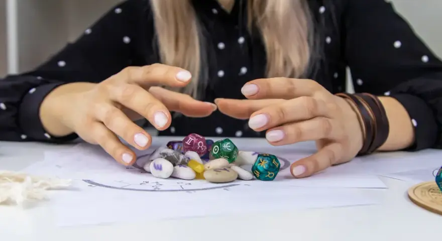 Dłonie nad kamieniami i kostkami z symbolami zodiaku. Czy wśród nich kryje się najsilniejszy znak zodiaku?