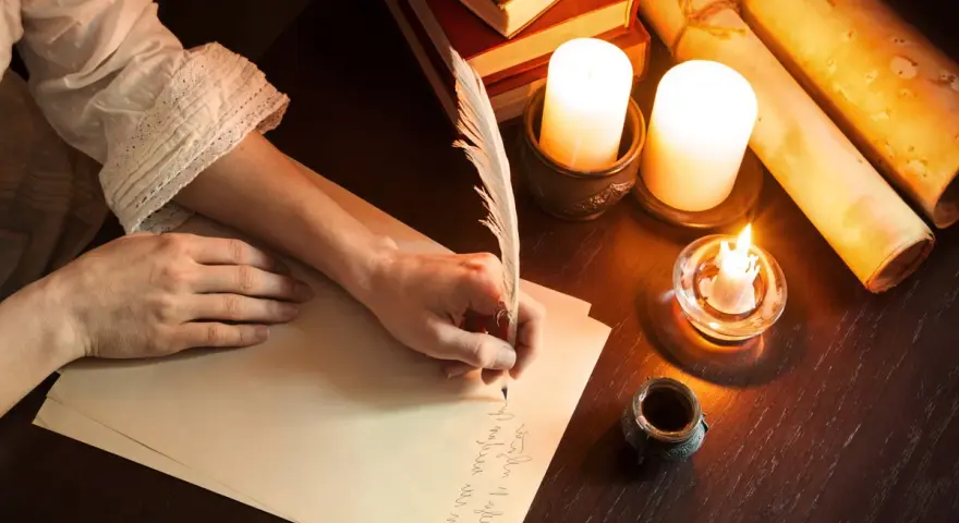 Ręka pisze piórem prośbę do anioła stróża. W blasku świec, wśród starych ksiąg i zwojów, powstaje list.