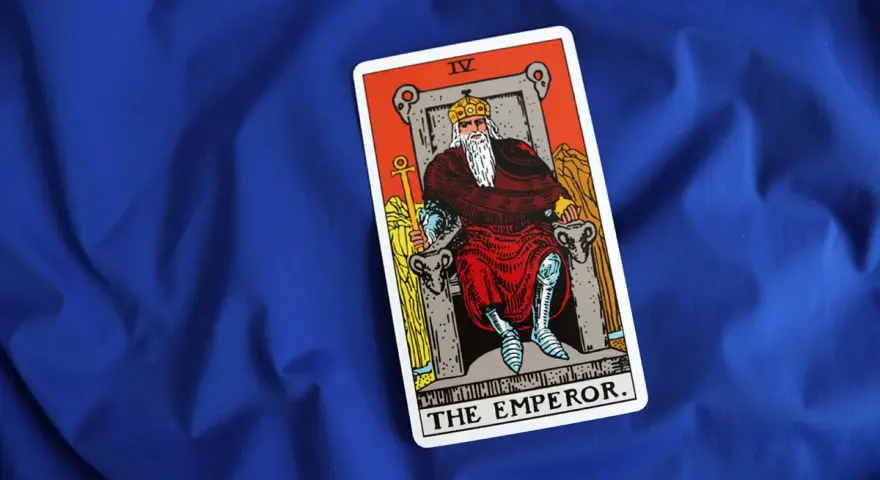 Karta cesarz tarot, przedstawiająca władcę na tronie, leży na niebieskim tle.