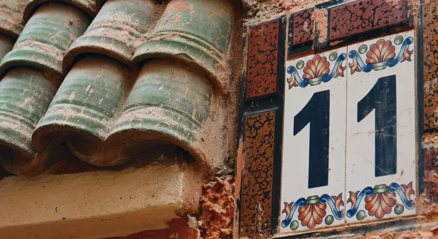 Numerologia partnerska 11 i 11. Dwa numery 11 na ozdobnych kafelkach, obok zielonych dachówek.