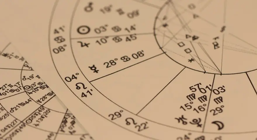 Zbliżenie na wykresy astrologiczne z symbolami planet i znaków zodiaku. Widoczny fragment horoskopu, gdzie 22.11 to znak zodiaku Strzelec.
