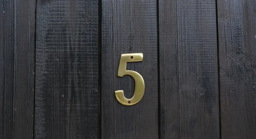 Złota cyfra 5 na ciemnej, drewnianej desce. Numerologiczna 3 i 5 symbolizują zmianę i wolność.